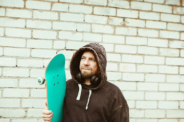 Portrait of adult 40 years man with red hair with blue skateboard, white brick wall background, outdoor