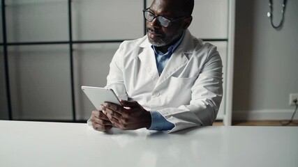 Aufkleber - Experienced medical professional in lab coat and glasses working with tablet computer at white desk, focusing intently during patient consultation in modern clinic setting