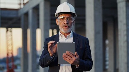 Poster - Experienced engineer wearing safety helmet and glasses holds tablet, gesturing and explaining project details at construction site in slow motion
