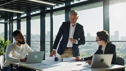 Poster - Senior engineer explaining project details to diverse colleagues during a meeting in a modern office, reviewing blueprints and using laptops in slow motion