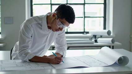 Poster - Engineer wearing protective safety glasses meticulously drawing technical blueprints while working at desk in modern bright office, focusing on precise architectural design project