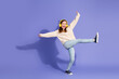 © deagreez - Joyful young girl dancing with headphones against a purple background in a stylish sweater and jeans