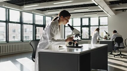 Poster - Laboratory research montage shows a female medical student using a microscope, conducting scientific analysis in a bright lab with colleagues working in the background, captured in slow motion