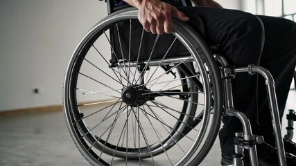 Poster - Close up slow motion of a man's hands pushing the wheels of his wheelchair in an empty room with large windows, conveying a sense of independence and mobility