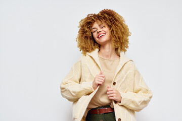 Wall Mural - Happy young woman with curly hair wearing a cream cardigan against a light background, smiling radiantly, creating a joyful and uplifting atmosphere perfect for fashion and lifestyle themes