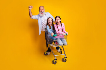 Poster - Excited grandfather pushes two happy young girls in a shopping cart against an energetic yellow background