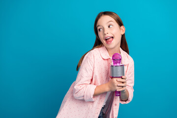 Wall Mural - Bright and cheerful girl singing with a pink microphone against blue background, showcasing joy and charisma