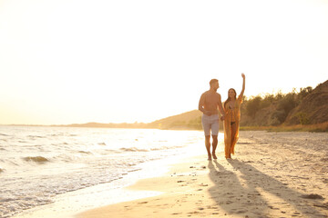 Wall Mural - Happy young couple running together on beach at sunset