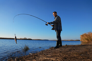 Wall Mural - Fisherman catching fish with rod at riverside