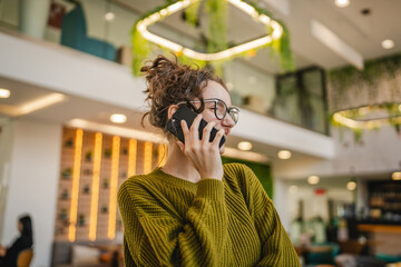 young happy woman student standing in a cafe and talk on mobile phone