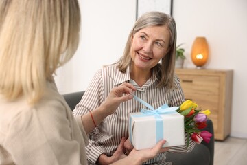 Wall Mural - Smiling mom receiving bouquet of tulips and gift from her daughter on sofa at home. Happy Mother's Day