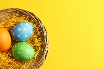 Wall Mural - Beautiful decorated Easter eggs in wicker bowl on yellow background, top view. Space for text