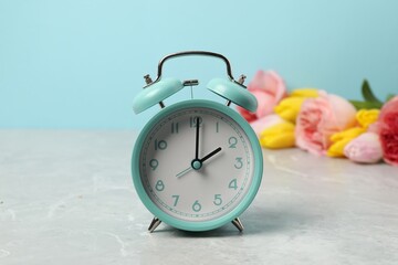 Aufkleber - Spring time. Alarm clock and beautiful flowers on grey marble table against light blue background
