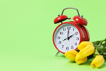 Poster - Spring time. Alarm clock and beautiful tulips on green background, space for text