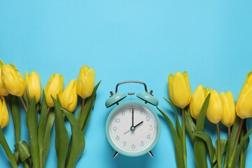 Poster - Spring time. Alarm clock and beautiful tulips on light blue background, flat lay. Space for text
