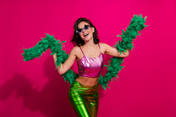 Wall Mural - Vibrant party fashion with a stylish woman posing with green boa on a bright pink background