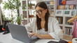 © Krakenimages.com - Young woman working on laptop in a home decor store with books, decorations, and plants in the background