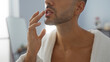 © Krakenimages.com - Handsome young man with a beard in a wellness center applying lip balm while wearing a white robe indoors