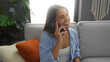 © Krakenimages.com - Young woman talking on phone in comfortable living room with vibrant cushions and indoor plants, projecting a relaxed and cheerful atmosphere.