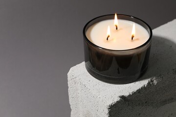 Wall Mural - Burning soy wax candle on concrete block against gray background, space for text