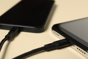 Wall Mural - USB charge cables connected to smartphones on beige background, closeup