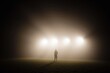 © velikiyzayats - A solitary figure stands amidst a foggy landscape, illuminated by bright lights in a mysterious setting, evoking feelings of intrigue and solitude at dusk.
