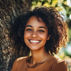 Poster - Smiling young woman with curly hair leaning against a tree in a sunlit outdoor setting during daytime. Generative AI