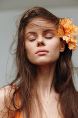 Canvas Print - Serene young woman with flowing hair and a flower in her hair, wearing an orange outfit, exudes natural beauty and calm emotions in a soft, pastel background.