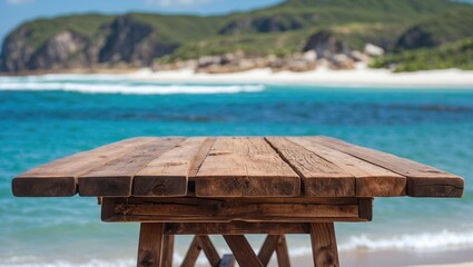 Poster - Wooden table on beach with blue ocean and green hills in background on sunny day