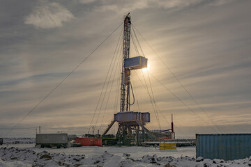 Wall Mural - Industrial winter landscape featuring an operational drilling rig with support facilities at a remote worksite during daylight hours