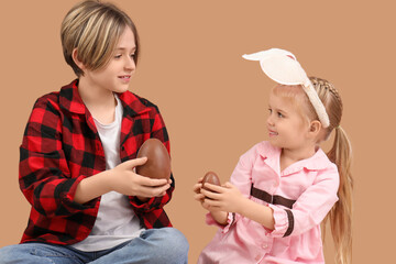 Wall Mural - Cute little children with chocolate eggs on brown background. Easter celebration