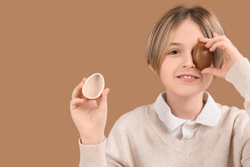 Wall Mural - Cute little boy with halves of chocolate egg on brown background. Easter celebration