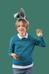 Wall Mural - Happy little boy in bunny ears with chocolate egg on green background. Easter celebration