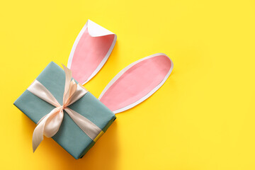 Wall Mural - Gift box with Easter paper bunny ears on yellow background