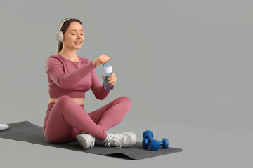 Wall Mural - Sporty young woman drinking water on grey background