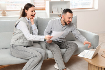 Wall Mural - Happy young couple with refund form and laptop sitting on sofa at home