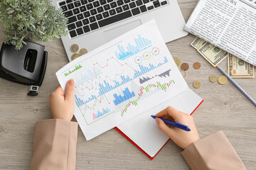 Wall Mural - Businesswoman with diagrams writing in notebook on light wooden table, top view. Financial Wellness Month