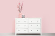 © Pixel-Shot - Vase with blooming branches and frame on commode near pink wall in room