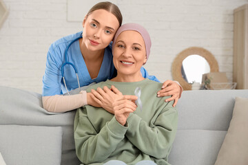 Wall Mural - Nurse hugging mature woman after chemotherapy on sofa at home. Brain cancer concept