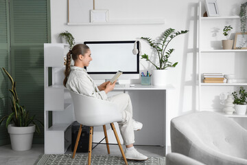 Wall Mural - Young woman with notebook sitting at table in office