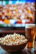 © Amanda - Bowl of popcorn and glass of beer on table with television in background watching sports game together friends enjoying movie night entertainment.