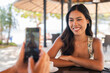 © Ranta Images - young woman on the beach smiling while friend taking photo of her with mobile phone