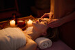 © AnnaStills - High angle of blonde woman lying on towel roll and getting facial massage by professional masseuse, room filling with aroma scent slowly