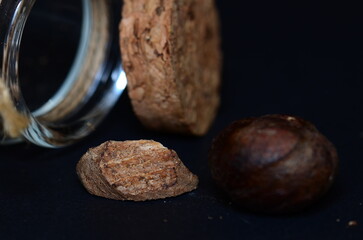 a culinary shot of nutmeg spice out of glass jar isolated on a black background.