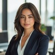 © DK Studio  - Portrait of a young Hispanic professional woman with warm brown eyes and sleek dark brown hair, wearing a tailored navy blazer and a white blouse. Confident businesswoman in modern office.