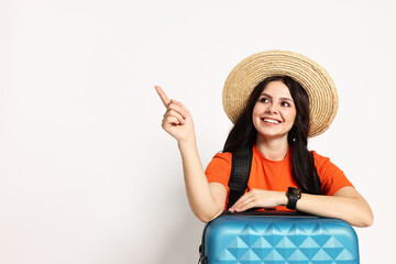 Sticker - Young tourist in hat with suitcase pointing at something on white background, space for text