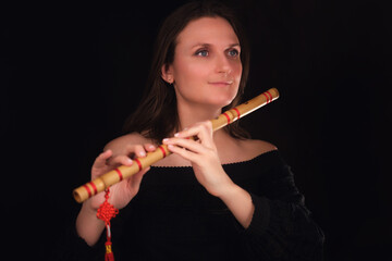 Woman holding wooden flute with red details. Studio portrait of female artist in black dress against dark background. Wind instrument and musical performance concept.