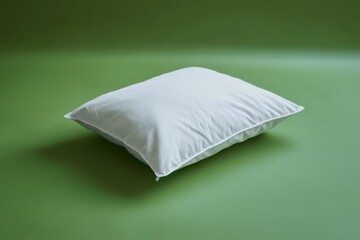 A white fluffy pillow lies on a solid green background surface