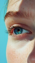 Aufkleber - A young female with striking blue eyes gazes thoughtfully, her fair skin illuminated by sunlight. The lively blue background enhances the allure of her captivating gaze