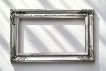 Poster - Elegant silver picture frame with ornate detailing against a white wall, catching soft natural light and creating subtle shadows, framing space.